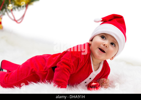 Happy smiling bébé couché sur le ventre et portant un chapeau de Père Noël Noël blanc et costume, isolé sur un fond blanc. Banque D'Images