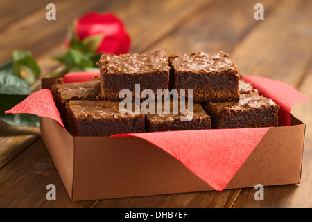 Brownies fraîchement cuits dans une boîte de papier brun avec une serviette rouge, avec rose rouge dans le dos Banque D'Images