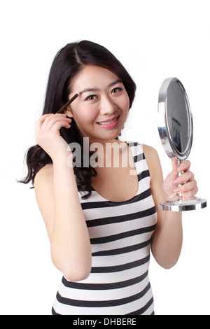 Jeune femme dans une robe rayée à la recherche dans un miroir,en appliquant le maquillage Banque D'Images