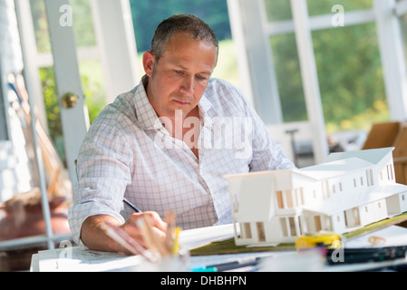 Une cuisine de la ferme. Un modèle d'une maison sur la table. La conception d'une maison. Un homme à l'aide d'un dessin au crayon sur un plan. Banque D'Images