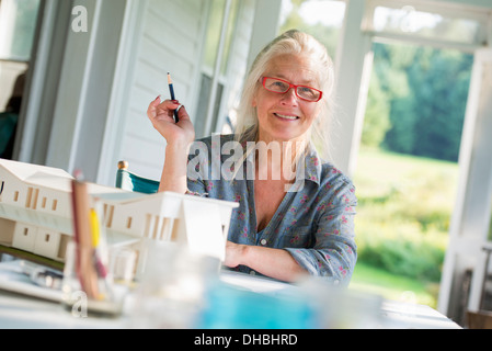 Une cuisine de la ferme. Un modèle d'une maison sur la table. La conception d'une maison. Une femme assise tenant un stylo. Banque D'Images