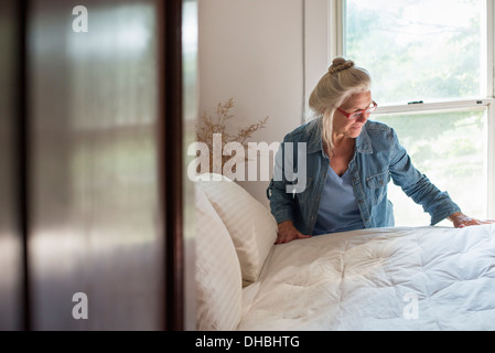 Une ferme à la campagne, une femme qui forment un lit dans une chambre. Banque D'Images