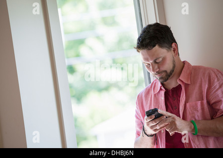 Un homme debout, dans un coin tranquille d'un café, à l'aide d'un téléphone intelligent. Banque D'Images