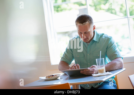 Un homme aux cheveux coupés court assis à une table de café. À l'aide d'une tablette numérique. Banque D'Images