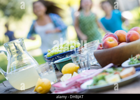 L'été un buffet de fruits et légumes, disposés sur une table. Les enfants s'exécutent en arrière-plan. Banque D'Images