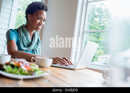 Une femme assise dans un café avec une tasse de café et un repas. À l'aide d'un ordinateur portable. Banque D'Images