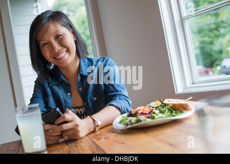 Une jeune femme à l'aide d'un smart phone, assis à une table. Le café et un sandwich. Banque D'Images