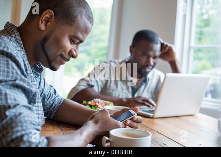 Deux hommes assis dans un café. À l'aide d'un ordinateur portable et un téléphone intelligent. Banque D'Images