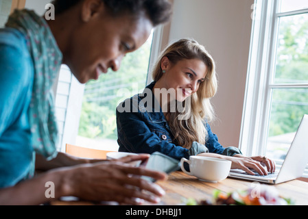 Deux femmes dans un café. À l'aide d'une tablette numérique et ordinateur portable. Travailler et rester en contact. Banque D'Images