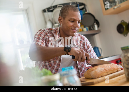 Un homme dans une cuisine de trancher une miche de pain. Banque D'Images