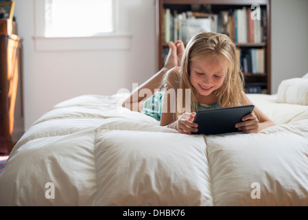 Une jeune fille assise sur son lit à l'aide d'une tablette numérique. Banque D'Images