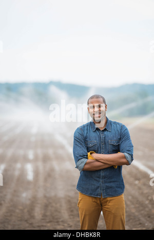 Une ferme maraîchère biologique, avec aspersion d'eau irrigation des champs. Un homme en vêtements de travail. Banque D'Images