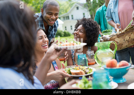 Un groupe d'adultes et de jeunes lors d'un repas dans le jardin d'une ferme. Plaques de passage et de lunettes. Banque D'Images