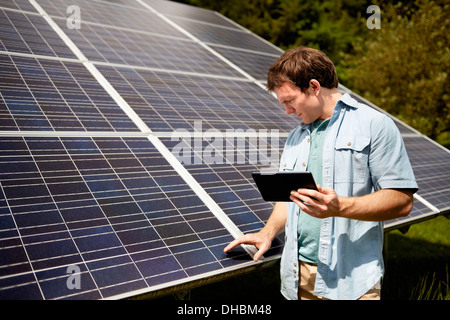 Un agriculteur en étroite collaboration l'inspection de la surface d'un panneau solaire sur la ferme. Banque D'Images