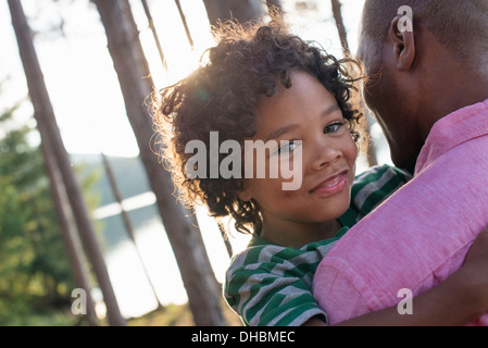 Des arbres sur les rives d'un lac. Un homme portant un enfant dans ses bras. Banque D'Images