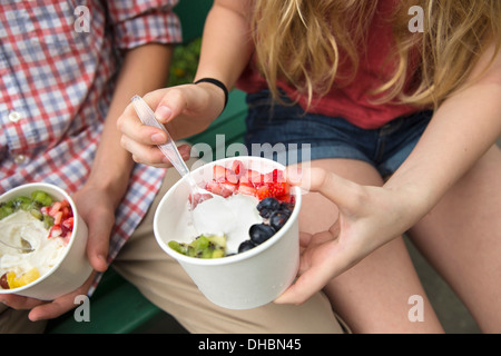 Les jeunes gens assis côte à côte, manger des fruits et yaourts désert. Banque D'Images