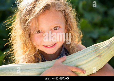 Une jeune fille avec de longs cheveux bouclés rouge à l'extérieur dans un jardin tenant un grand épi de maïs frais. Banque D'Images