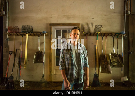 Une ferme biologique dans les Catskills. Un homme debout dans une grange avec de l'équipement entreposé autour des murs. Banque D'Images