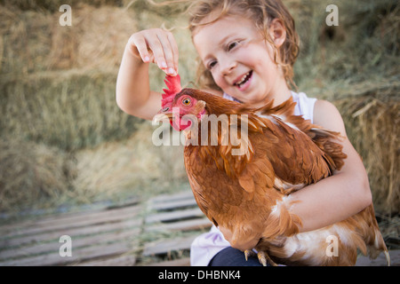 Une jeune fille tenant une poule dans un poulailler. Banque D'Images