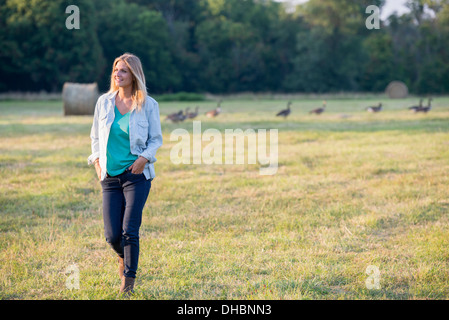 Une femme marchant sur un terrain, à l'écart d'un troupeau d'oies à l'extérieur l'air frais. Banque D'Images