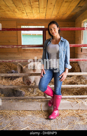 Une ferme biologique dans les Catskills. Une femme à côté d'un cochon dans un stylo, debout dans une paille. Banque D'Images