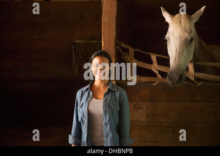 Une ferme biologique dans les Catskills. Une femme debout dans un environnement stable, avec un cheval blanc à la recherche sur le décrochage. Banque D'Images