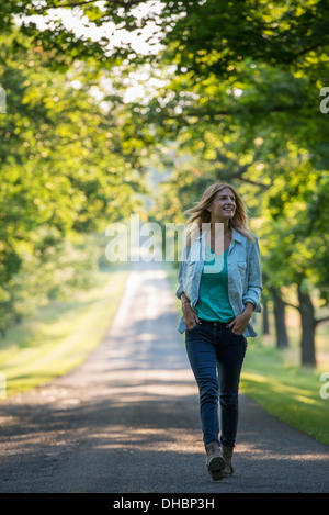 Une femme marchant dans un chemin bordé d'arbres. Banque D'Images