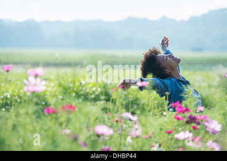 Une femme debout au milieu des fleurs avec ses bras tendus. Fleurs cosmos rose et blanc. Banque D'Images