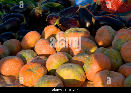 Spectacle coloré de citrouilles orange et violet profond aubergines en vente à Puttaparthi village market dans le soleil du matin. Banque D'Images