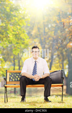Smiling young woman sitting on a bench and looking at camera dans un parc par une journée ensoleillée Banque D'Images
