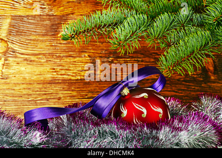 Décoration de Noël. Balle rouge avec ruban violet, de sapin et de guirlandes. Selective focus Banque D'Images