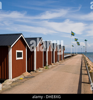 Une rangée de hangars à bateaux sous une rangée de drapeaux suédois à la marina à Båstad, la Suède. Banque D'Images