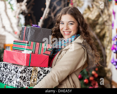 Femme portant des cadeaux de Noël empilés en magasin Banque D'Images