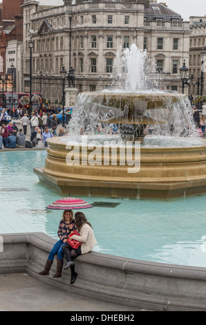 2 deux filles chat sous la pluie sous un parapluie à Trafalgar Square de Londres. Banque D'Images