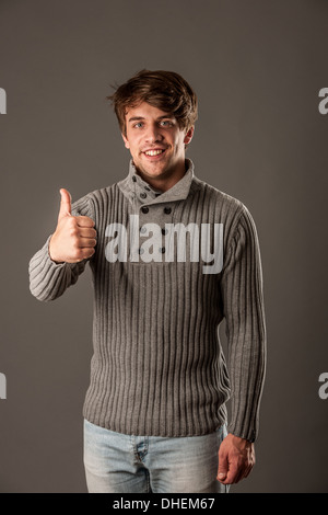 Heureux jeune homme de chandail gris showing thumb up Banque D'Images