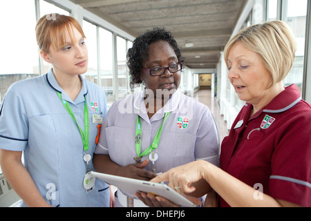 Trois infirmières utilisent un iPad pour regarder un patients note UK Banque D'Images