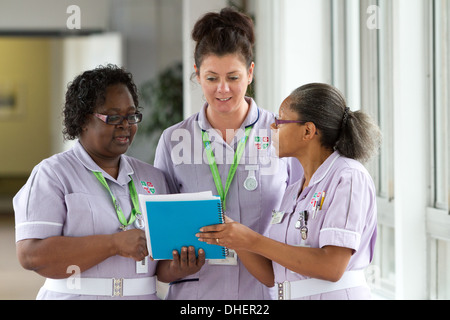 Un groupe de trois infirmières discuter un travail notes patients UK Banque D'Images