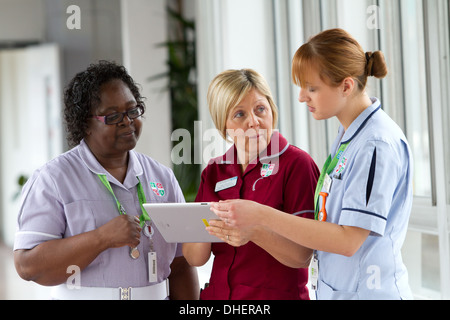 Un groupe de trois infirmières discuter de travailler sur un ordinateur tablette UK Banque D'Images