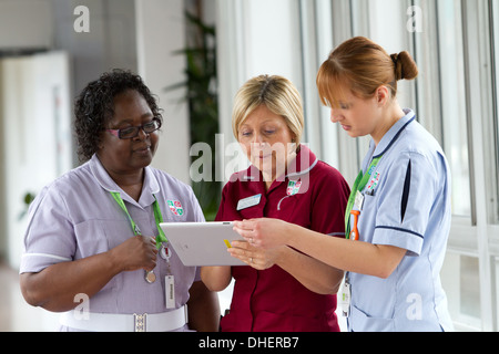Un groupe de trois infirmières discuter de travailler sur un ordinateur tablette UK Banque D'Images