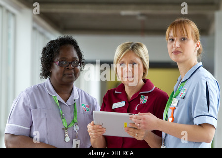 Un groupe de trois infirmières discuter de travailler sur un ordinateur tablette UK Banque D'Images