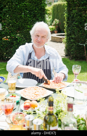 Senior man wearing apron cutting pizza Banque D'Images