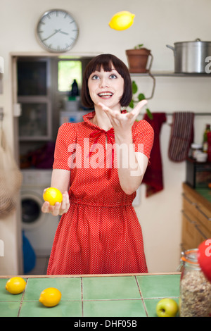 Young woman in kitchen juggling citrons Banque D'Images