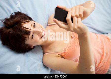 Overhead view of young woman on bed taking self portrait Banque D'Images