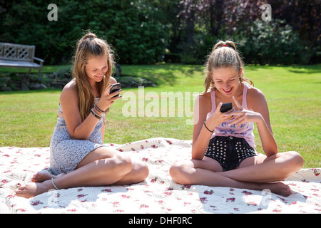 Deux adolescentes sur couverture de pique-nique à la recherche de téléphones mobiles
