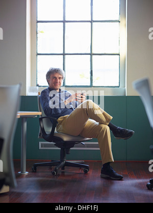 Mature businessman sitting on office chair wit cell phone Banque D'Images
