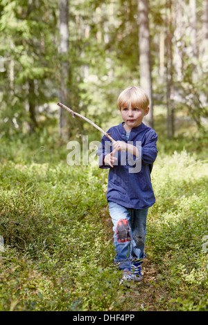 Boy walking through forest exerçant son stick Banque D'Images