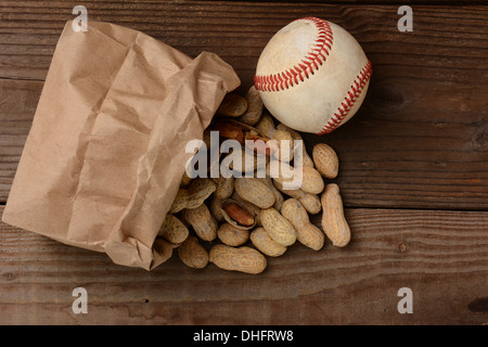 Un sac d'arachides et un base-ball sur un vieux banc en bois au stade de baseball. Le sac en papier est sur le côté avec les écrous. Banque D'Images