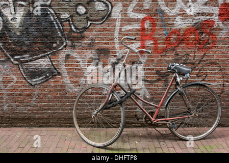 Un vieux vélo s'appuya contre un mur de graffiti'd dans le centre d'Amsterdam, aux Pays-Bas. Banque D'Images