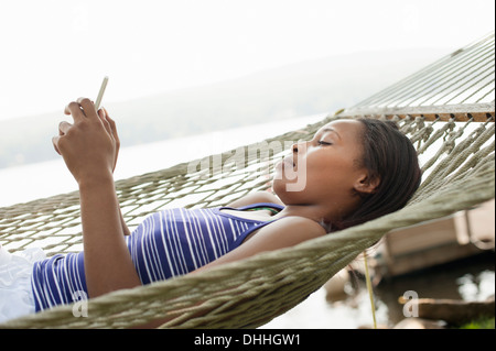 Young woman lying in hammock using cell phone Banque D'Images