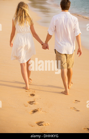 Romantic couple holding hands walking on beach au coucher du soleil. L'homme et de la femme dans l'amour. Des empreintes de pas dans le sable. Banque D'Images